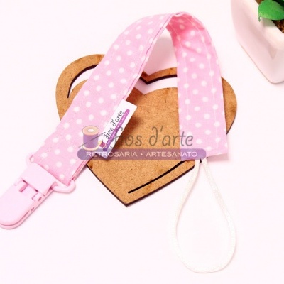 Prendedor de chuchas rosa com bolinhas brancas e etiqueta, sobre madeira em forma de coração, ao lado de vaso com planta