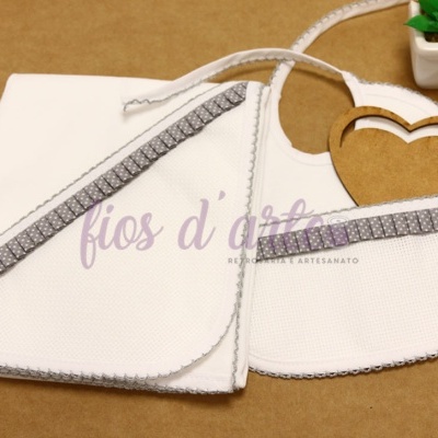 Babete e toalha brancos com bordas cinza sobre superfície castanha com planta em vaso branco