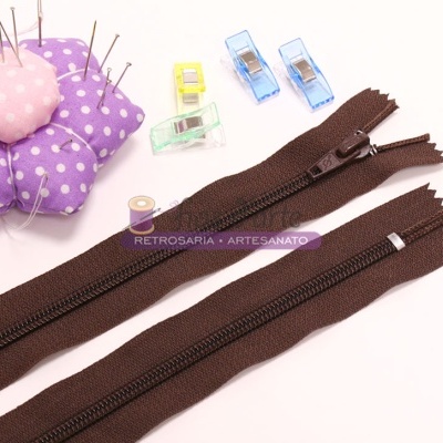 fechos éclair marrons, almofada de alfinetes roxa com pontos brancos, bobina de linha e pregadores coloridos