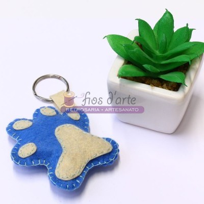 Porta-chaves em forma de pata de cão azul e bege junto a planta artificial num vaso branco