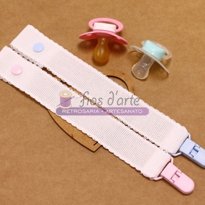 Dois porta-chupetas elásticos branca com fecho rosa e azul com duas chupetas coloridas sobre superfície castanha