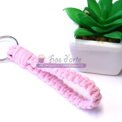 Porta-chaves rosa trançado com argola metálica ao lado de vaso branco com planta artificial verde