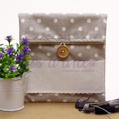 Bolsa de tecido bege com bolinhas brancas e botão de madeira ao lado de vaso branco com flores roxas