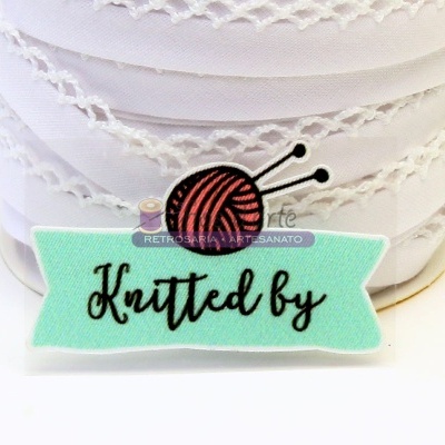 fita branca bordada com etiqueta 'Knitted by' e novelo de lã