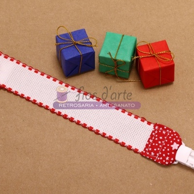 Fita para chupeta branca com bordas vermelhas e padrão de estrelas, ao lado de três pequenos presentes coloridos