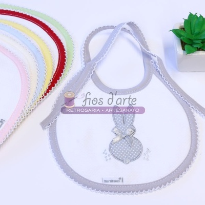 Babetes de tecido com borda em renda e estampa de coelhos em várias cores em fundo branco com planta suculenta