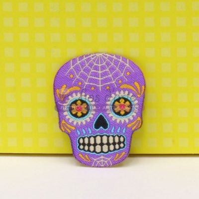 Figura decorativa de caveira colorida com padrão de teia de aranha num fundo amarelo