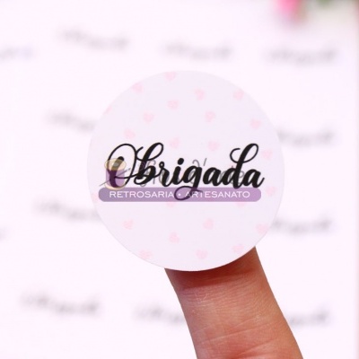 Adesivo redondo branco com texto Obrigada e Retrosaria e Artesanato segurado no dedo