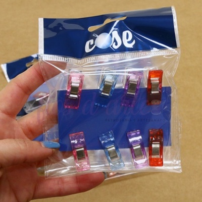 Embalagem com oito molas coloridas em cartão azul, sendo segurada por uma mão.