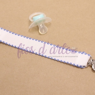 Prendedor de chupeta com clip em forma de coração metálico e fita branca com borda azul.