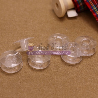 Cinco bobinas de plástico transparente sobre superfície castanha com fita xadrez ao fundo