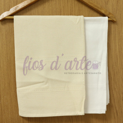 Dois panos de cozinha com padrão waffle, um cru e outro branco, pendurados em cabide de madeira