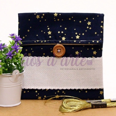 Estojo azul escuro com estrelas douradas e bordado, junto a planta artificial e novelos de linha dourada