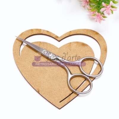 Tesoura prateada pequena sobre base de madeira em formato de coração com flores cor-de-rosa ao lado