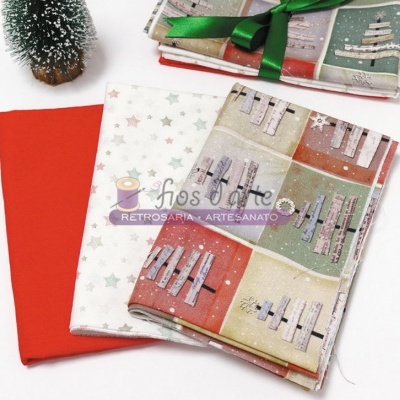 Três tecidos natalícios dobrados com padrões coloridos e um tecido vermelho liso, com pinheiro artificial ao lado