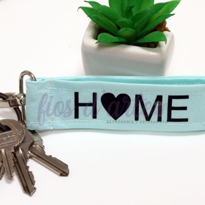 Porta-chaves azul claro com texto e três chaves, e planta artificial ao fundo