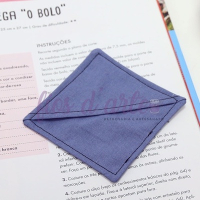 Estojo quadrado em tecido azul com costura em losango sobre página impressa em português
