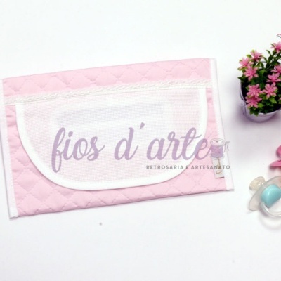 Carteira rosa acolchoada com bolso branco, texto 'fios d'arte', vaso de flores cor-de-rosa e duas chupetas coloridas ao lado