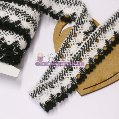 Fita de renda preta e branca com padrão zig-zag e pompons sobre suporte de coração em madeira