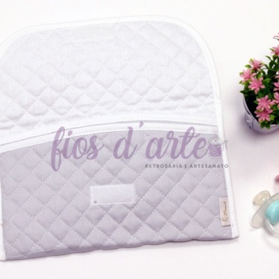 Estojo almofadado cinzento e branco junto a planta e chupetas.