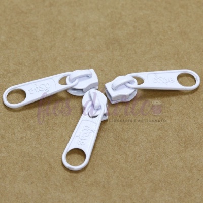 Três puxadores de fecho éclair brancos com inscrição RIRI sobre fundo castanho.