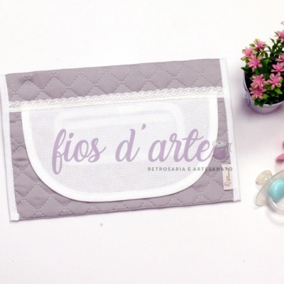 Pano cinza com renda e texto, vaso com flores cor-de-rosa e três chuchas coloridas