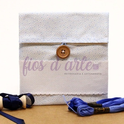 Envelope artesanal bege com botão de madeira e linha azul sobre mesa