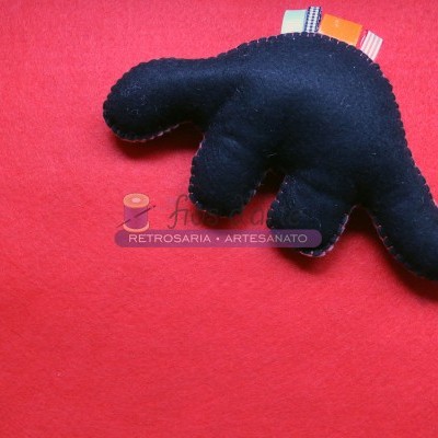 Pelúcia artesanal preta com formato de dinossauro sobre fundo vermelho