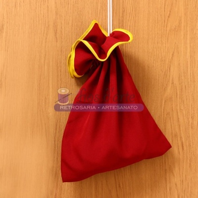 Saco vermelho com bordas amarelas pendurado numa superfície de madeira.