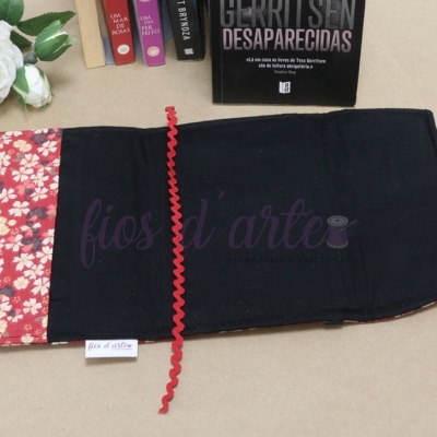Capa de livro em tecido preto e floral com fita vermelha sobre fundo bege com flores brancas