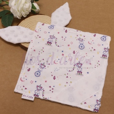 Pano de bebé branco com padrão colorido e orelhas, sobre fundo castanho com flores e madeira.