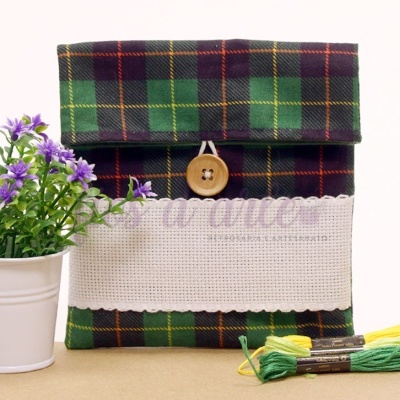 Bolsa xadrez verde com botão e faixa branca, flores roxas em vaso branco, novelos de linha verde e amarelo