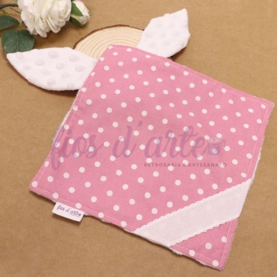 Lenço rosa com pintas brancas e orelhas brancas texturizadas sobre superfície castanha com flor e madeira