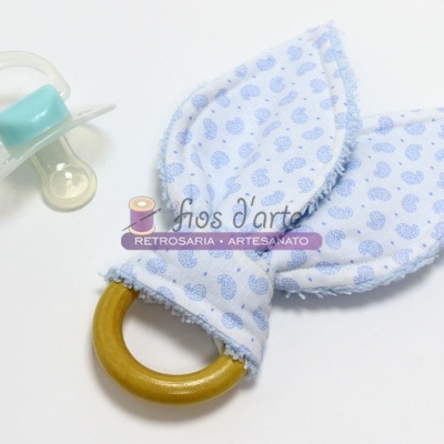 Anel de dentição com tecido azul claro e chucha azul claro sobre superfície branca