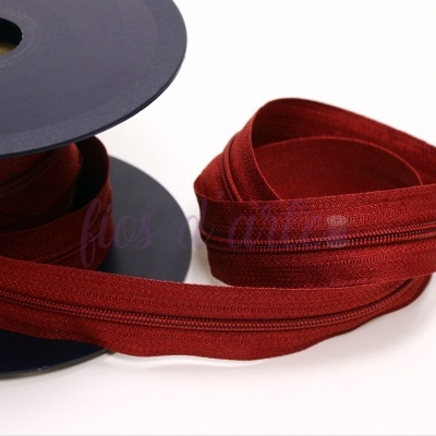 Rolo de fita zíper vermelho borgonha com textura de tecido sobre fundo branco