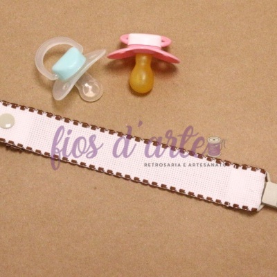 Pacificador para bebé com clipe, fita bege e dois biberões de silicone azul e rosa numa superfície castanha