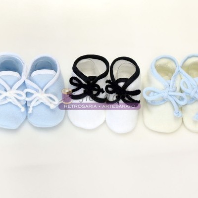 Três pares de sapatinhos de bebé em tecido felpudo, azul claro, branco com atacadores pretos e branco com atacadores azuis