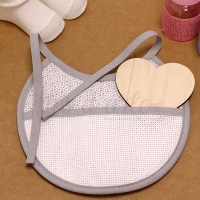 Babete para bebé em tecido branco e cinzento com acessórios para bebé à volta sobre superfície castanha.