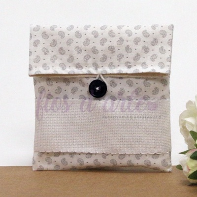 Bolsa de tecido bege com padrão de folhas e botão preto sobre superfície castanha com flores brancas