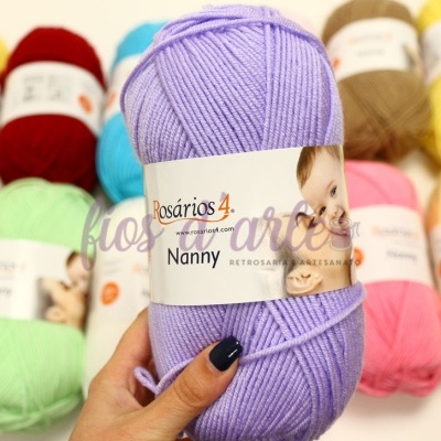 Novelo de lã roxo claro da Rosários 4 Nanny segurado pela mão, com vários novelos coloridos ao fundo.