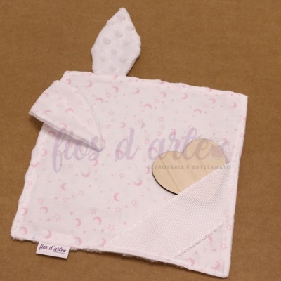 Pano branco com estampas rosas e detalhe em forma de orelha, junto a um coração de madeira clara.