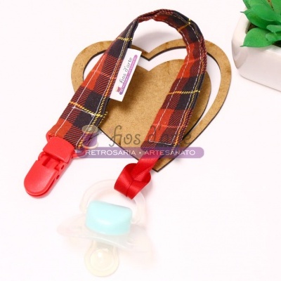 Prendedor de chucha em tecido xadrez vermelho com clips vermelhos ao lado de planta artificial