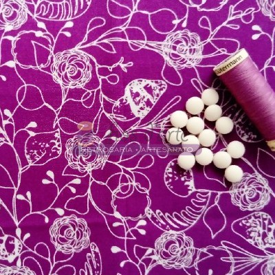 tecido roxo com padrão floral branco, botões brancos e carretel de linha roxa