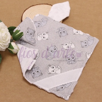 Bandana cinzenta para bebé com desenhos de cães e etiqueta branca, junto a flor branca e madeira