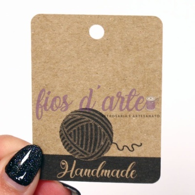 Etiqueta de cartão marrom com ilustração de novelo e texto 'fios d'arte Handmade'
