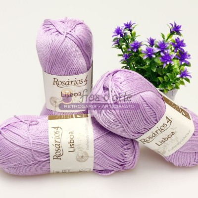 Três novelos de lã lilás claro e um pequeno vaso com flores lilás