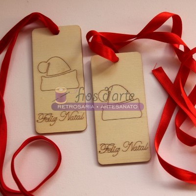 Etiquetas de madeira com desenhos de gorro de Natal e texto Feliz Natal, com fitas vermelhas.