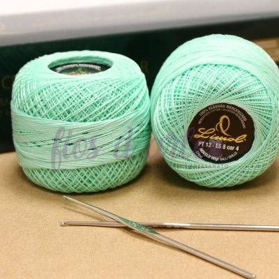 Dois novelos de linha de croché verde água com agulhas de croché em superfície bege