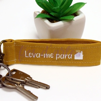 Porta-chaves de tecido amarelo com frase e imagem de uma cama, com chaves e vaso com planta