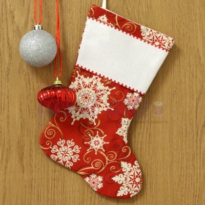 Meia de Natal vermelha com flocos de neve brancos pendurada numa superfície de madeira com duas bolas de Natal ao lado